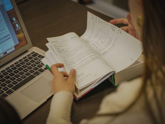 Étudiante consulte un livre devant son ordinateur